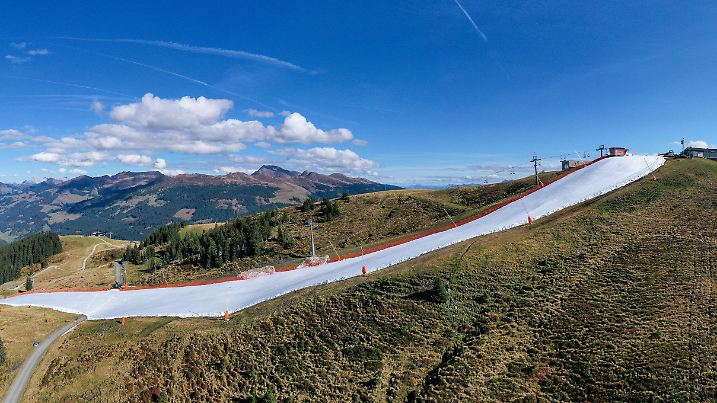 18.10.2019, Österreich, Mittersill: Für eine schmale Piste wurde konservierter Schnee aus dem vergangenen Winter als Band in der Berglandschaft auf der noch grünen Resterhöhe in den Kitzbüheler Alpen aufgetragen. Die Bergbahnen Kitzbühel gehen das fünfte Jahr in Folge schon im Oktober in Betrieb. Der frühe Saisonstart für Skifahrer sorgt für Streit in Österreich.  (zu dpa "Blick über die Grenze") Foto: Expa/Johann Groder/APA/dpa +++ dpa-Bildfunk +++
