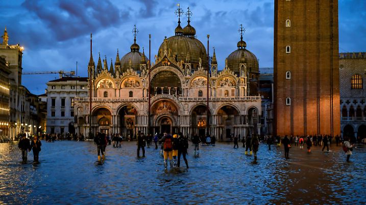 18.11.2019, Italien, Venedig: Touristen stehen auf dem überschwemmten Markusplatz. Der Hochwasserstand hat heute eine neue Spitze erreicht. Venedig ist zum dritten Mal innerhalb einer Woche überflutet worden. Am Sonntag sei das Wasser auf 150 Zentimenter über den normalen Meeresspiegel gestiegen, erklärte Bürgermeister Brugnaro. Foto: Claudio Furlan/LaPresse via ZUMA Press/dpa +++ dpa-Bildfunk +++