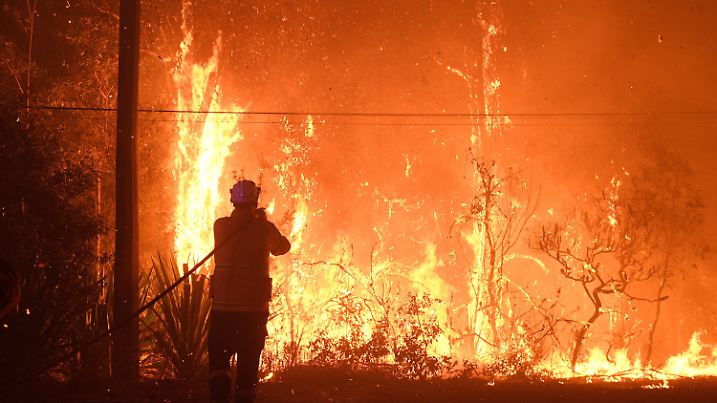 05.12.2019, Australien, Sydney: Ein Feuerwehrmann der New South Wales Feuerwehrbehörde versucht Häuser an der Waratah Road und der Kelyknack Road vor dem Feuer zu schützen. Wegen der nahen Buschbrände ist Australiens Ostküstenmetropole erneut in Rauch gehüllt worden. Foto: Dan Himbrechts/AAP/dpa +++ dpa-Bildfunk +++