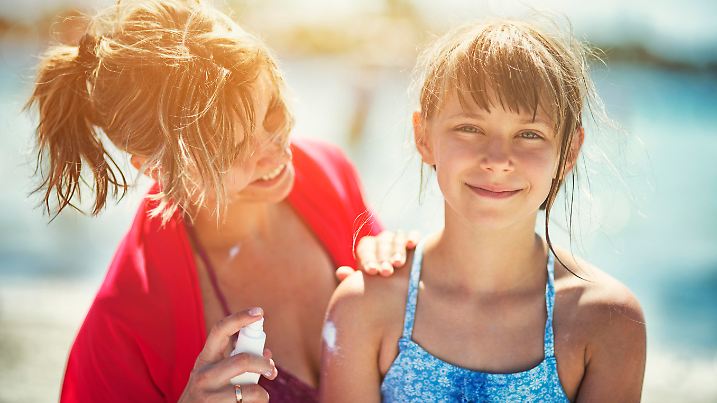 Mother and daughter on beach. Mother is applying sunscreen lotion on her daughter. The girl is aged 8. 