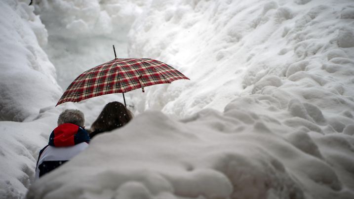 10.02.2021, Italien, Cortina d'Ampezzo: Ski alpin, Weltmeisterschaft: Fußgänger sind im Zentrum zwischen Schneemassen von Cortina unterwegs. Nach heftigem Schneefall wurden der Wettkampftag komplett abgesagt. Der Skiort ist Austragungsstätte für die Olympischen Winterspiele die 2026 in Mailand und Cortina d'Ampezzo stattfinden. Foto: Michael Kappeler/dpa +++ dpa-Bildfunk +++
