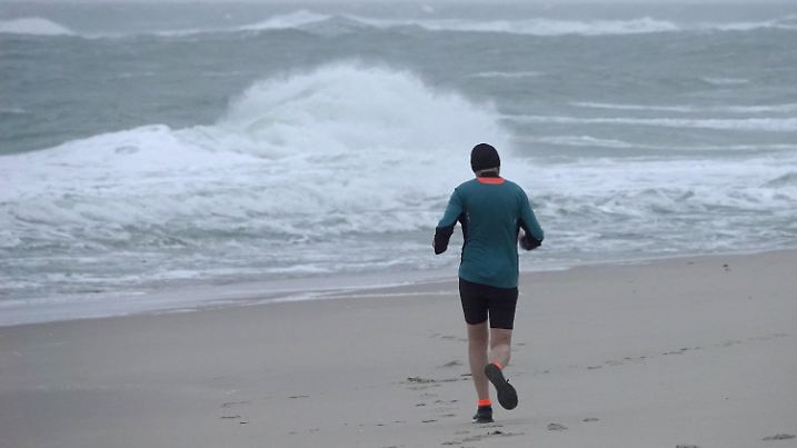 02.11.2020, Schleswig-Holstein, Westerland: Ein Jogger ist bei stürmischem Wetter am Morgen am Strand von Westerland unterwegs. Bund und Länder haben ab Montag wegen der Corona-Pandemie einen Teil-Lockdown beschlossen. In Schleswig-Holstein müssen Touristen grundsätzlich bis zum 2. November abgereist sein, Urlauber auf den Nordsee-Inseln und Halligen bekommen wegen der Kapazitäten im Fährverkehr sowie den Autozügen bis zum 5. November Zeit. Foto: Bodo Marks/dpa +++ dpa-Bildfunk +++