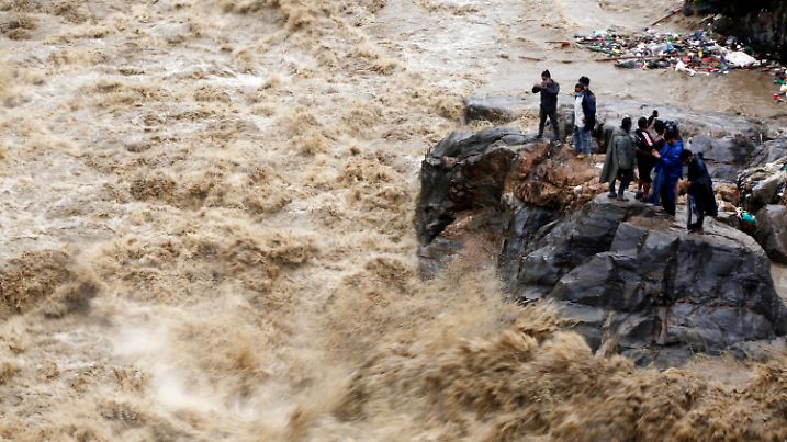 ARCHIV - 21.07.2020, Nepal, Kathmandu: Nepalesen stehen auf einem Felsen am Ufer des überfluteten Flusses Bagmati und fotografieren die Strömung. Heftiger Monsunregen hatte in Nepal, Indien und Bangladesch zu mehr als 200 Toten geführt und Tausende Menschen obdachlos gemacht. Vier von fünf Naturkatastrophen sind nach einer Studie des Roten Kreuzes in den vergangenen zehn Jahren auf extremes Wetter und die Folgen der Klimakrise zurückgegangen. Dazu gehören Unwetter, Überschwemmungen und Hitzewellen. (zu dpa: "Rotes Kreuz: Mehr Katastrophen durch Klimawandel und Extremwetter") Foto: Niranjan Shrestha/AP/dpa +++ dpa-Bildfunk +++