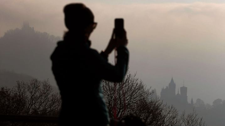 27.11.2020, Nordrhein-Westfalen, Königswinter: Eine Frau fotografiert mit dem Smartphone Nebelschwaden, die im Rheintal am Schloss Drachenburg (r) und dem Drachenfels (l) vorbeiziehen. Foto: Oliver Berg/dpa +++ dpa-Bildfunk +++