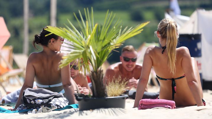 04.07.2019, Nordrhein-Westfalen, Essen: Unter einer Minipalme sonnen sich vier junge Leute im Freibad "Beachside" am Baldeneysee. Das sommerliche Wetter mit Temperaturen bis 30 Grad soll in NRW weiter anhalten. Foto: Roland Weihrauch/dpa +++ dpa-Bildfunk +++
