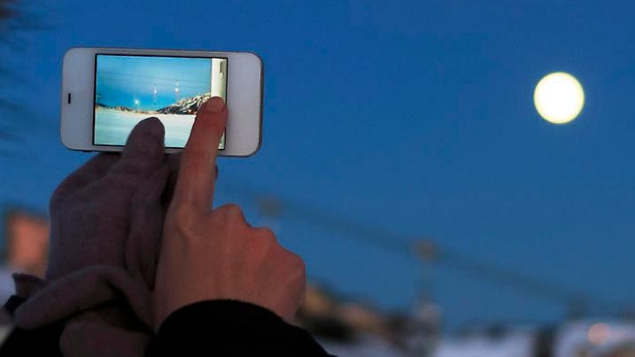 Girl photographing the moon with a touch screen phone. Ski resort. Beautiful nature in a twilight time.