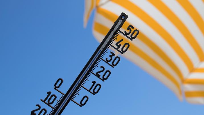 thermometer shows over thirty degree celsius with yellow striped sunshade and blue sky
