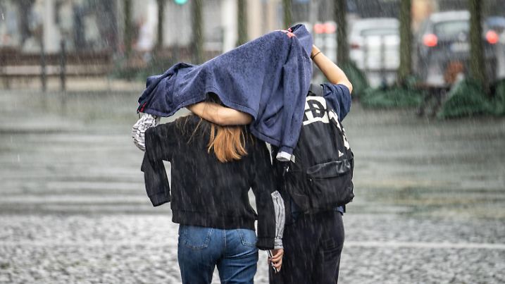 11.07.2021, Hessen, Frankfurt/Main: Zwei Passanten schützen sich mit einer Jacke vor einem der zahlreichen Regenschauer, die am Sonntag in der Mainmetropole das Wetter bestimmten. Foto: Frank Rumpenhorst/dpa +++ dpa-Bildfunk +++