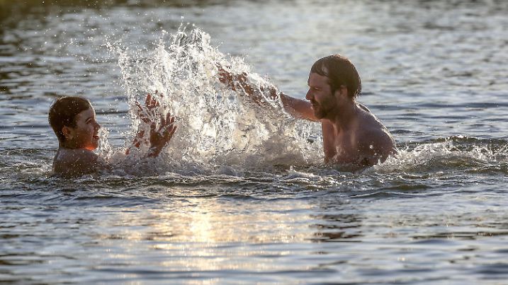 24.06.2020, Baden-Württemberg, Ertingen: Ein Vater und sein Sohn spritzen sich im Gegenlicht der aufgehenden Sonne in einem Badesee mit Wasser an. Foto: Thomas Warnack/dpa +++ dpa-Bildfunk +++