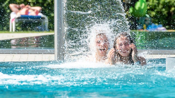 24.07.2019, Bayern, Passau: Lena und Jonas kühlen sich unter einem Wasserfall im Freibad «peb» ab. Deutschland steht eine Hitzewelle bevor - und schon am Mittwoch wird diese in vielen Gebieten deutlich spürbar. Foto: Armin Weigel/dpa +++ dpa-Bildfunk +++