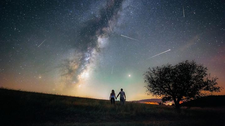 Young man and woman under the bright night sky watching the milky way and Perseid meteor shower