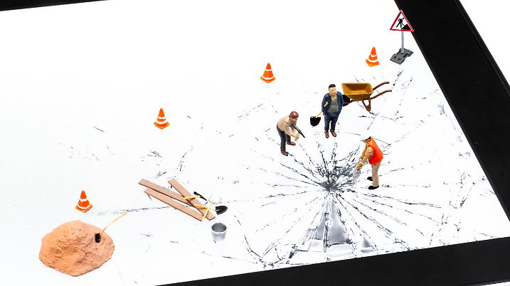Digital tablet with broken glass and miniature of manual workers that trying to repair the glass. 