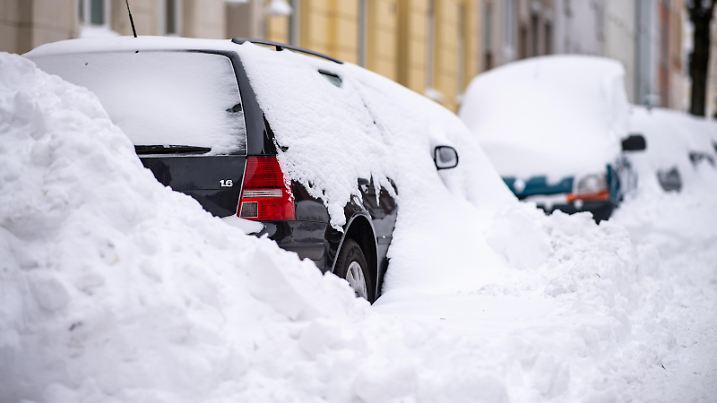 Durch das räumen der Schneemassen auf den Straßen, stehen eingeschlossene parkende Autos am Straßenrand.