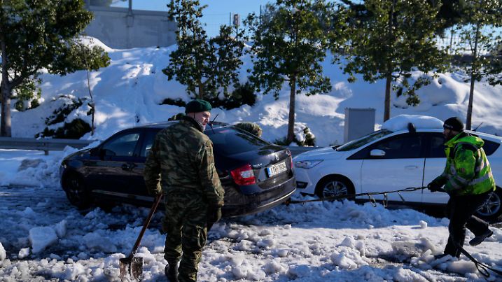 26.01.2022, Griechenland, Athen: Zwei griechische Soldaten versuchen ein im Schnee festgefahrenes Auto auf der Autobahn Attiki Odos zu befreien. In Griechenland hat es nach den starken Schneefällen der vergangenen Tage weiterhin große Probleme gegeben. Foto: Thanassis Stavrakis/AP/dpa +++ dpa-Bildfunk +++