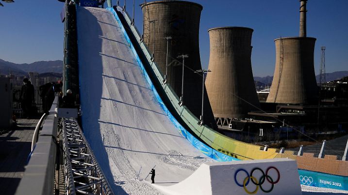 01.02.2022, China, Beijing: Ein Arbeiter formt den Kicker auf dem Big Air Shougang im Vorfeld der Olympischen Winterspiele 2022. Im Hintergrund sind die alten Kühltürme eines Stahlwerks im ehemaligen Industriegebiet der Stadt zu sehen. Die Olympischen Winterspiele in Peking finden vom 04.-20.02.2022 unter strengen Corona-Auflagen statt. Foto: Jae C. Hong/AP/dpa +++ dpa-Bildfunk +++