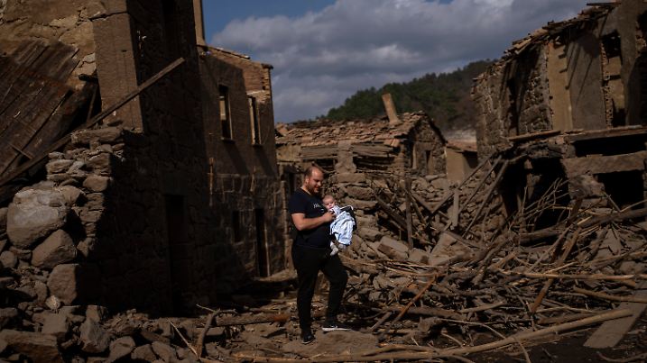 Rafael Monlina, 33, holds his four-month-old son Marcos as they visit the old village of Aceredo, submerged three decades ago when a hydropower dam flooded the valley, emerged now due to drought at the Lindoso reservoir, in northwestern Spain, Saturday, Feb. 12, 2022.  (AP Photo/Emilio Morenatti)