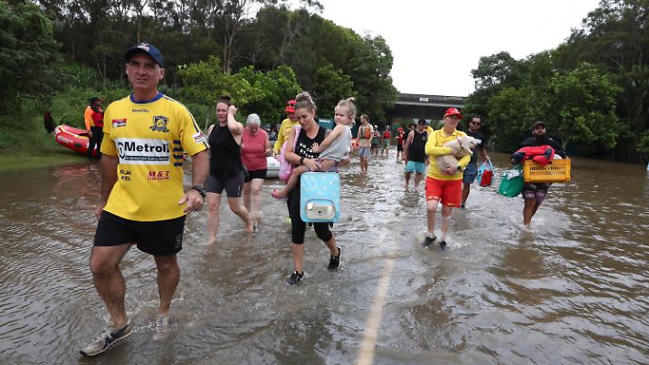 dpatopbilder - 01.03.2022, Australien, Chinderah: Menschen gehen auf einer überschwemmten Straße. Viele Menschen vor allem rund um die Stadt Lismore im Bundesstaat New South Wales seien vor den schnell steigenden Wassermassen auf die Dächer ihrer Häuser geflohen und warteten dort auf Hilfe, sagte der australische Premierminister Scott Morrison am 28.02.2022. Foto: Jason O·brien/AAP/dpa +++ dpa-Bildfunk +++