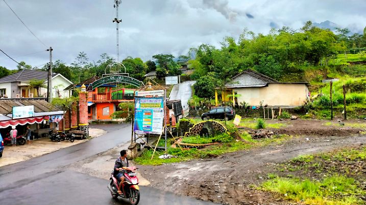 10.03.2022, Indonesien, Sleman: Ein Mann fährt auf einem Motorrad an einer Straße vorbei, in deren Hintergrund der nebelverhangene Berg Merapi zu sehen ist, gesehen vom Dorf Cangkringan in Sleman, Yogyakarta. Der indonesische Vulkan Merapi stieß in der Nacht zum Donnerstag heiße Wolken aus, die etwa 250 Bewohner zur Flucht in Notunterkünfte zwangen. Es wurden keine Todesopfer gemeldet. Foto: Slamet Riyadi/AP/dpa +++ dpa-Bildfunk +++