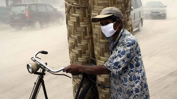 An Indonesian man wears protective mask as he carries woven bamboo walls on his bike on a ash covered motorway after mount Merapi erupted in Yogyakarta, Indonesia, 30 October 2010. Indonesia's Mount Merapi volcano with 2,968 meters high in Central Java erupted again, spewing hot ashes as high as 2 kilometers, covering up the radius of 10 kilometers around the mountain, official said. Mount Merapi first erupted on 26 October, killing at least 33 people and displacing over 40,000 others. EPA/HADI SUSANTO +++(c) dpa - Bildfunk+++