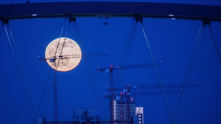 18.03.2022, Hessen, Frankfurt/Main: Der Mond steht über Offenbach am Main. Dabei sind im Vordergrund Baukräne und der Rohbau eines Häuserkomplexes zu sehen. Foto: Boris Roessler/dpa +++ dpa-Bildfunk +++