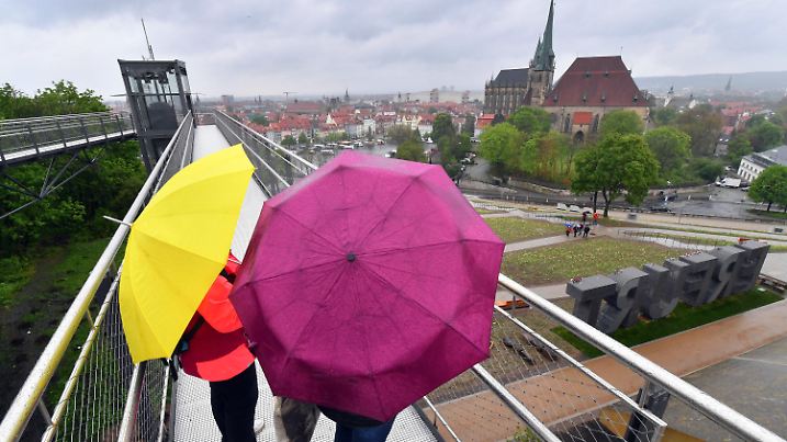 12.05.2021, Thüringen, Erfurt: Besucherinnen der Bundesgartenschau (BUGA) stehen bei Regenwetter auf dem Petersberg mit Blick auf die Stadt mit Mariendom und Severikirche. Vom 23. April bis 10. Oktober 2021 findet das Sommerfest mit gärtnerischer Leistungsschau auf zwei Ausstellungsflächen in Erfurt statt. Dazu kommen 25 BUGA-Außenstandorte in ganz Thüringen. Foto: Martin Schutt/dpa-Zentralbild/dpa +++ dpa-Bildfunk +++