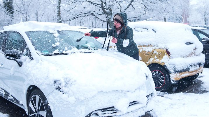 Eine Frau reinigt bei Schneefall ihr Auto.