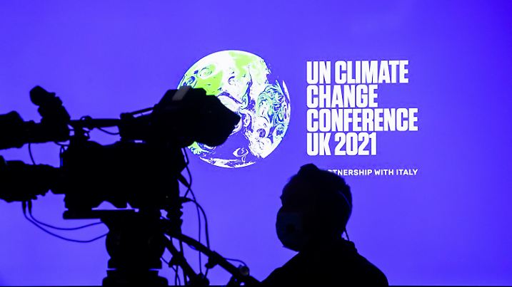 ARCHIV - 09.11.2021, Großbritannien, Glasgow: Ein Kameramann steht bei der UN-Klimakonferenz COP26 in Glasgow vor einem Bildschirm mit dem Weltklimakonferenz-Logo. (zu dpa: «WMO: 1,5-Grad-Schwelle könnte bis 2026 erstmals überschritten werden») Foto: Christoph Soeder/dpa +++ dpa-Bildfunk +++