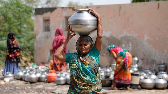 10.05.2022, Indien, Ahmedabad: Eine Frau aus einem Slum trägt einen Wasserkrug auf den Kopf, in dem sich Trinkwasser aus einem Brunnen einer Tempelanlage befindet. Foto: Ajit Solanki/AP/dpa +++ dpa-Bildfunk +++