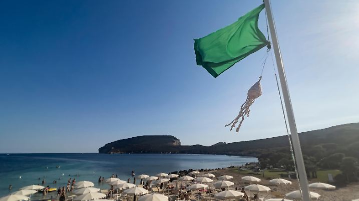 Eine gestrickes Modell einer Meduse flattert im Wind unter einer gruenen Fahne, am Mittwoch, 20. Juli 2022 an einem Strand bei Alghero auf Sardinien, Italien. Die Fahne zeigt den Badegaesten an, ob Medusen im Wasser eine Gefahr fuer die Badenden darstellen oder ob die Situation sicher ist. Aufgrund der waermeren Wassertemperaturen und der aermeren Fischbestaende haben sich die Medusen im Mittelmeer vermehrt und vergaellen vielen Touristinnen und Touristen die Badeferien. (KEYSTONE/Alessandro della Valle)