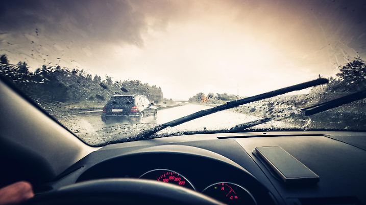 A car driving through a rainy highway with the windshield wipers in motion.