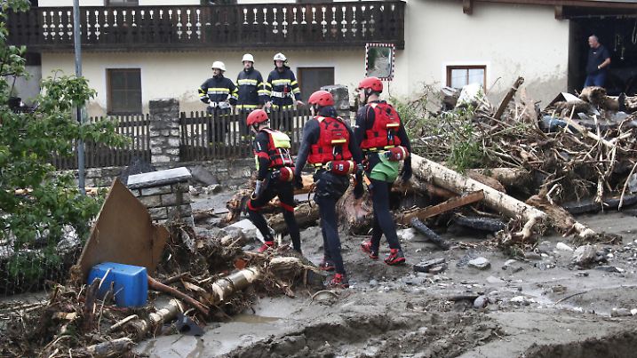 29.06.2022, Österreich, Treffen: Feerwehrleute beobachten Einsatzkräfte des Katastropfenschutz bei ihren Arbeiten nach einem Unwetter mit schweren Schäden. Schwere Unwetter haben ganze Ortschaften im Bezirk Villach-Land verwüstet. Bäche traten über die Ufer und verschütteten die Häuser teils bis zum ersten Stock. Besonders betroffen war das Gegendtal. In Treffen am Ossiacher See und in der Gemeinde Arriach wurde noch in der Nacht eine Zivilschutzwarnung ausgegeben. Foto: Gert Eggenberger/APA/dpa +++ dpa-Bildfunk +++