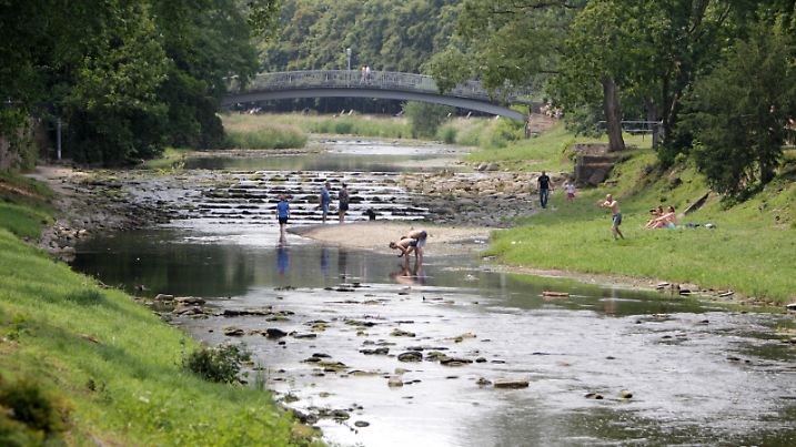 Menschen genießen am 05.07.2015 am grünen Ufer der Ahr in Bad Neuenahr-Ahrweiler (Rheinland-Pfalz) das sommerliche Wetter und kühlen sich im Wasser ab. Foto: Fredrik von Erichsen/dpa ++