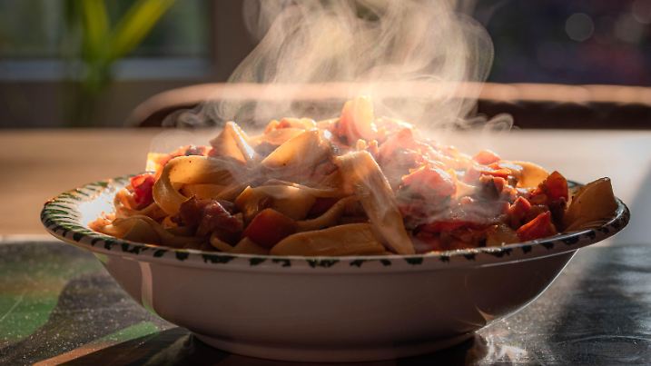 Berlin, Deutschland 29. September 2021: Einer Teller mit Nudeln, Pasta, steht dampfend auf einem Esstisch. Auf den Nudeln liegen Tomaten- und Paprikastückchen mit einer Soße.