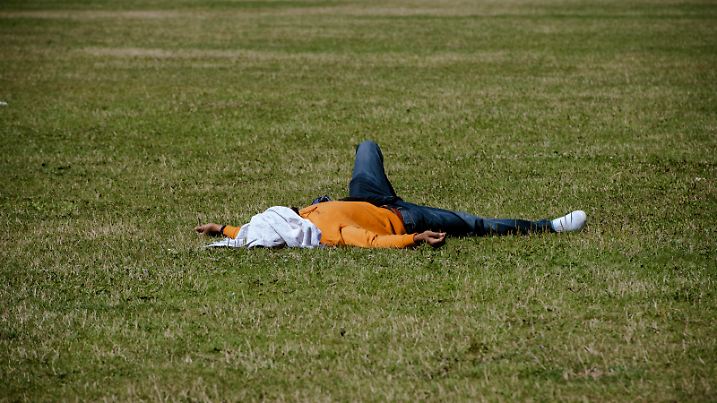 Ein Mann liegt auf einer Wiese im Regierungsviertel und schützt sein Gesicht mit einem Shirt vor den Sonnenstrahlen.