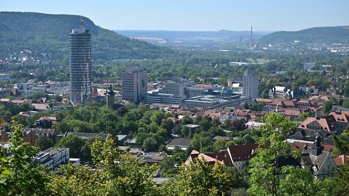 19.07.2022, Thüringen, Jena: Dunst liegt über der Stadt an einem heißen Sommertag. Mehr große Bäume ins Stadtgebiet zu bringen, ist in Jena ein wichtiger Teil der städtischen Klimastrategie. Die Stadt setzt inzwischen auch auf mediterranen Sorten, zum Beispiel den aus dem Süden stammenden und Hitze gewohnten Zürgelbaum. Foto: Martin Schutt/dpa +++ dpa-Bildfunk +++