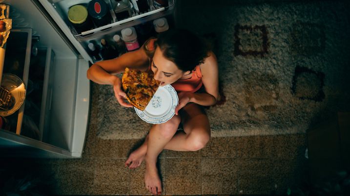 Woman eating in front of the refrigerator in the kitchen late night
