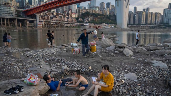 20.08.2022, China, Chongqing: Menschen sitzen in einem flachen Wasserbecken im Flussbett des Jialing-Flusses, eines Nebenflusses des Jangtse, in der südwestchinesischen Stadt Chongqing. Die Landschaft von Chongqing, einer Millionenstadt, zu der auch das umliegende Ackerland und die steilen und malerischen Berge gehören, wurde durch eine ungewöhnlich lange und intensive Hitzewelle und eine damit einhergehende Dürre verändert. (zu dpa: «China kämpft wegen Dürre und Hitze mit Stromknappheit») Foto: Mark Schiefelbein/AP/dpa +++ dpa-Bildfunk +++