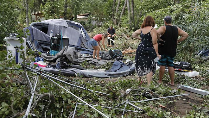 18.08.2022, Frankreich, Coggia: Camper packen die Reste ihrer zerstörten Zelte und anderen Gegenstände auf dem Campingplatz Sagone ein, wo ein Baum während der Stürme auf der französischen Mittelmeerinsel Korsika auf einen Bungalow gestürzt ist. Bei heftigen Unwettern sind im Mittelmeerraum und in Österreich mehrere Menschen getötet worden. Auf der französischen Mittelmeerinsel Korsika kamen gestern einige Menschen ums Leben. Foto: Pascal Pochard-Casabianca/AFP/dpa +++ dpa-Bildfunk +++