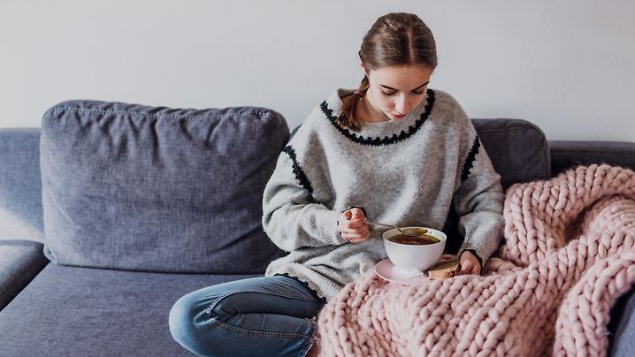 junge Frau sitz auf Sofa und isst Suppe (Foto: picture alliance / Mikelo / VisualEyze) || Modellfreigabe vorhanden