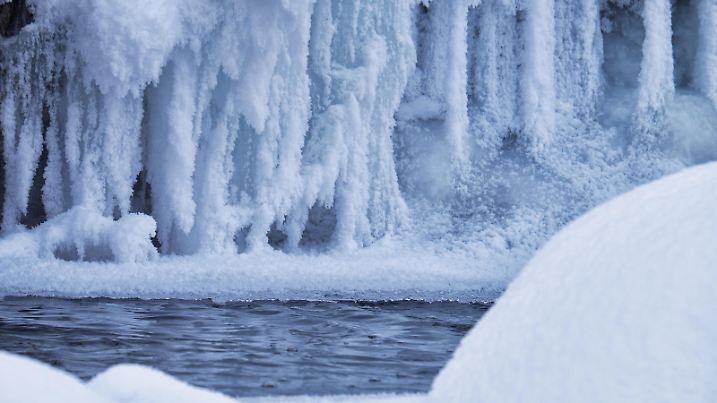 Photo of icicles Stones with snow caps and ice in the water of frozen river Pescherka near waterfall in winter season. Siberia, Russia