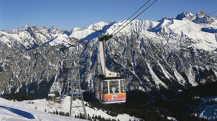 Eine mit Menschen beladene Gondel fährt in einem Schneegebit die Berge hoch.