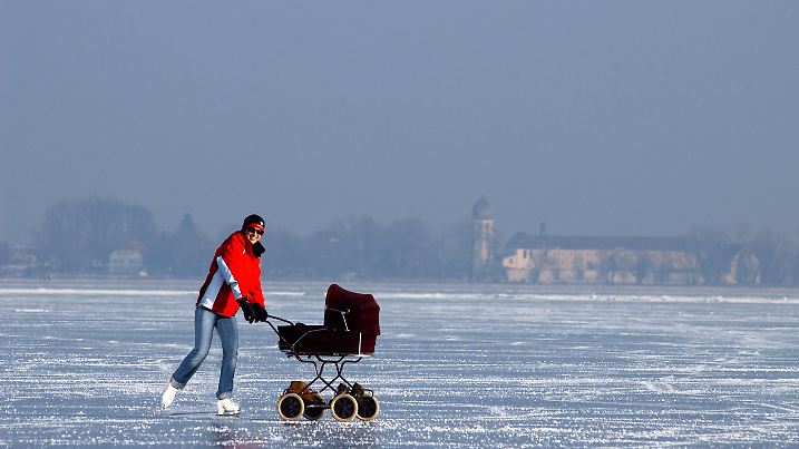 Den zugefrorenen Chiemsee bei Rimsting (Oberbayern) nutzt am Donnerstag (08.01.2009) diese Frau, um mit Schlittschuhen und Kinderwagen den Winter zu genießen. Im Hintergrund ist das Kloster Frauenchiemsee der Benediktinerinnenabtei Frauenwörth zu seh