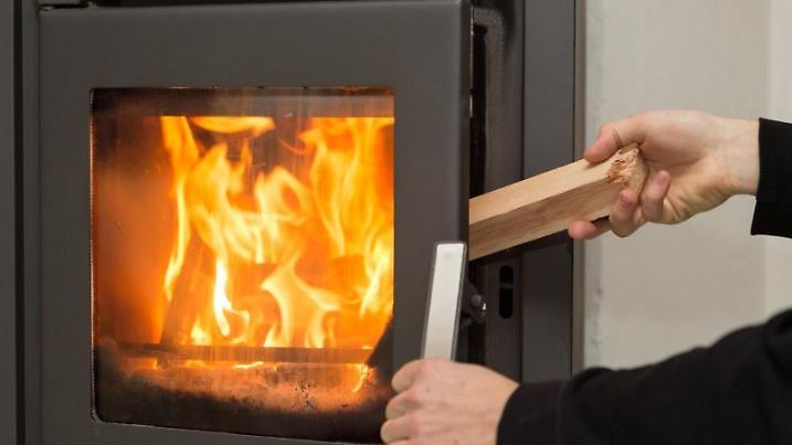 Man legt Holz in brennenden Kaminofen