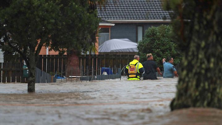 26.01.2023, Neuseeland, Auckland: Rettungskräfte und ein Mann waten durch das Hochwasser einer überschwemmter Straße. Nach massiven Regenfällen stehen weite Teile Aucklands unter Wasser. Die Bürger der Metropole wurden vom Zivilschutz aufgefordert, sich in Sicherheit zu bringen. Foto: Hayden Woodward/New Zealand Herald/AP/dpa +++ dpa-Bildfunk +++