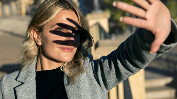 portrait of blonde woman facing the sun making shadow with her hand on her face revealing a green eye