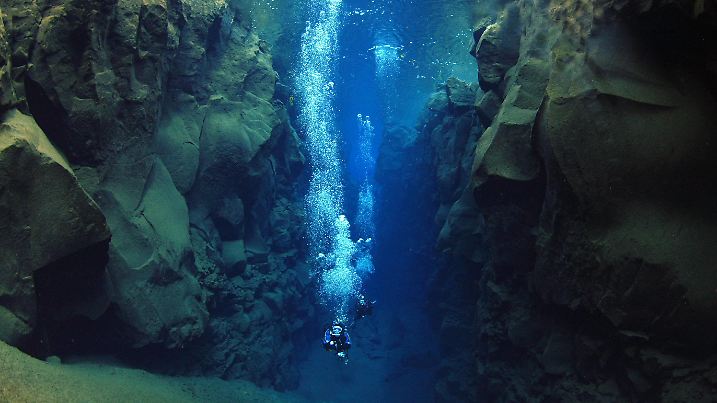 Picture shows two divers exploring the Silfra Gap so called by locals in Iceland. The fault that is ever widening is the divide between East & West perhaps in all senses of the phrase. America and Europe are slowly separating by the rate of about 2cm per annum. As they do, the earth's tectonic plates open up to producing gigantic cracks. These cracks in turn expose huge boulders - the very core of the earth. Most of the time they appear underwater and hidden from view, however, occasionally these cracks can be observed on land. Iceland straddles the rift, which is responsible for separating the Americas from Europe and straight through her middle lies the fault line. Thus Iceland provides a unique opportunity to witness this geological phenomenon at first hand. Due to its location around one third of Iceland is covered by glaciers. In the warmer summer months melt water filters through Iceland's porous volcanic rock on its journey towards the sea. In doing so, this virtually pure water is super filtered. For the majority of the time this filtered water remains underground. However, where the faults or cracks have appeared they are filled by the melt water. This produces an underwater Mecca for divers in search for the clearest water in the world. The water is so clear that for all intense and purposes it has infinite visibility. Some divers complain of suffering from vertigo as they are deprived of their sense of depth. Diving in this cold (2-4°C) lifeless water you are literally swimming between two continents. America is on one side and Europe on the other. No film set could produce this spectacle. At the bottom of the crack there are only two sounds. One is the noise of your bubbles as you breath, the other is of a low frequency rumble reminding you that the separation continues. Date: 27/04/2005 Ref: ZB775_109049_0194 COMPULSORY CREDIT: Oceans Image/Photoshot