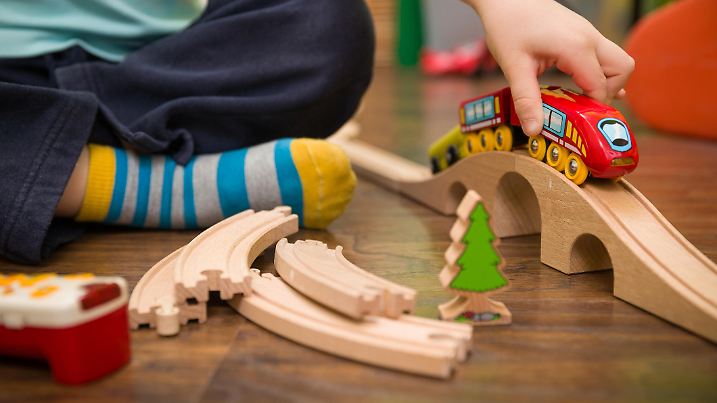 Close up on child's hands with toy train and railway in his room. Boy playing indoors.