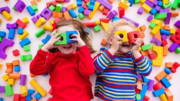Happy preschool age children play with colorful plastic toy blocks. Creative kindergarten kids build a block tower. Educational toys for toddler or baby. Top view from above.