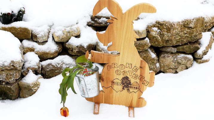 Holz-Osterhase im Schnee mit der Aufschrift: FROHE OSTERN - Ein ploetzlicher Winter- und Kaelteeinbruch bedeckt die Landschaft mit einer Schneedecke. - Schnee, Frost und Eis zum kalendarischen Fruehlingsbeginn an diesem Dienstag, dem 20. Maerz 2018, nahezu in ganz Deutschland. Es herrschen trotz erster Fruehlingstage immer noch sehr winterliche Wetterverhaeltnisse.