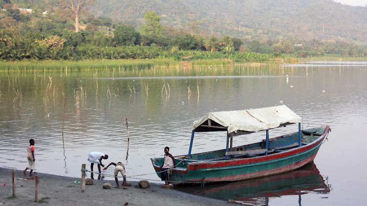 Kinder spielen neben einem Boot am Nordufer des Lake Bosomtwe (Lake Bosumtwi) in der Ashanti Region von Ghana am 22.01.2014. Der ehemalige große Meteoritenkrater besitzt keine Zu- und Abflüsse. Foto: Rolf Zimmermann